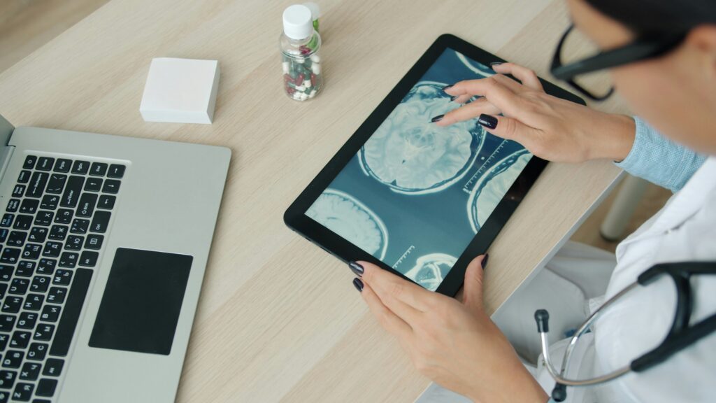 Doctor examining digital brain scans on a tablet, demonstrating how AI in healthcare supports human clinical decision-making.